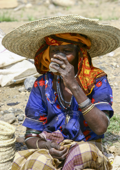 Yemeni woman with straw hat in traditional clothing drinking, Taiz Governorate, Jabal Sabir, Yemen