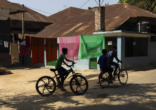 Bangladeshi boys riding bicycles and with laundry put up on washing lines, Rajshahi Division, Manda, Bangladesh