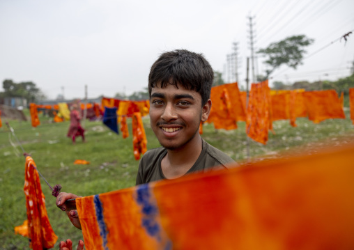 Bangladeshi smiling worker drying orange fabrics under the sun, Dhaka Division, Rupganj, Bangladesh
