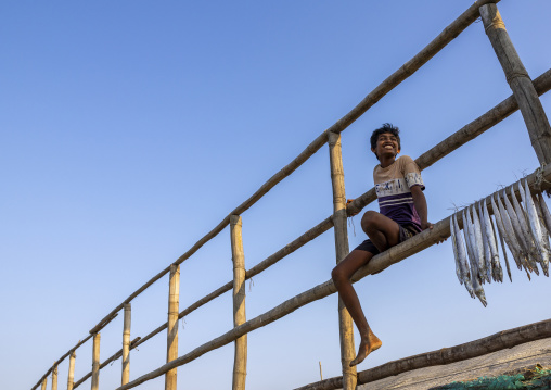A young bangladeshi worker laids out fish to dry in sun on drying rack, Chittagong Division, Cox's Bazar Sadar, Bangladesh