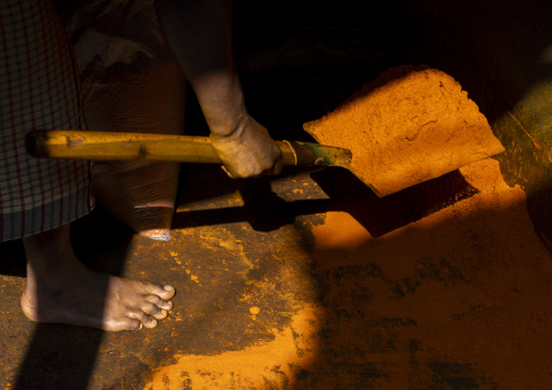 Man picking up turmeric orange powder with a shovel in a mill, Dhaka Division, Dhaka, Bangladesh