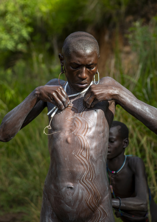 Shepherd from suri tribe receiving help to paint his body, Tulgit, Omo valley, Ethiopia