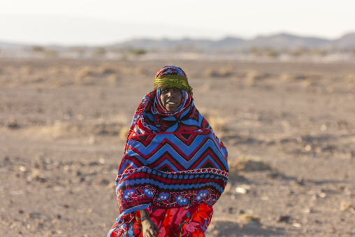 An Afar woman wrapped in a colorful patterned shawl stands in the desert, Afar depression, Lake Abbe, Djibouti