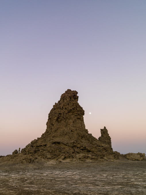 A full moon rises beside a towering limestone chimney at dusk, Afar depression, Lake Abbe, Djibouti