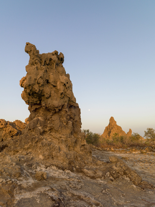 A full moon hovers above a solitary limestone chimney rock formation, Afar depression, Lake Abbe, Djibouti