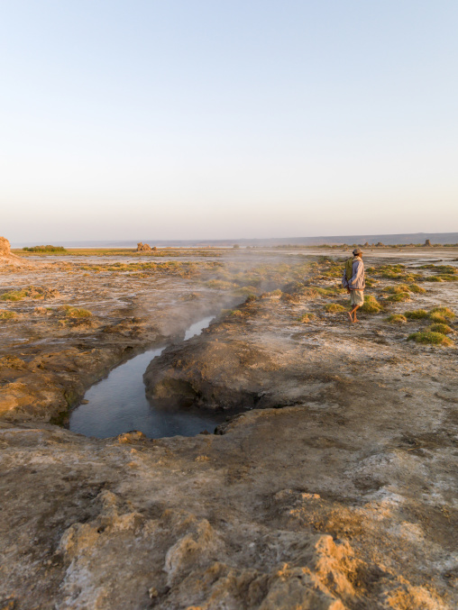 A man walks past a steaming hot spring on the salt flat, Afar depression, Lake Abbe, Djibouti