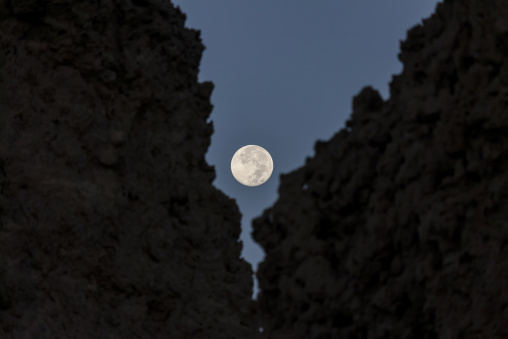 A full moon glows between two dark limestone chimney silhouettes, Afar depression, Lake Abbe, Djibouti