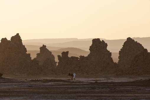 Three tourists walk among towering limestone chimney rock formations at sunset, Afar depression, Lake Abbe, Djibouti