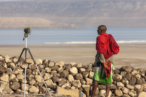 An afar man in observes the lake through a spotting scope beside a stone wall, Afar depression, Lake Abbe, Djibouti