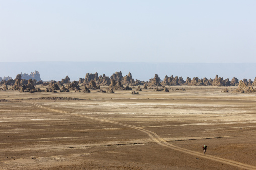 A lone traveler walks across the cracked desert plain toward distant limestone spires, Afar depression, Lake Abbe, Djibouti