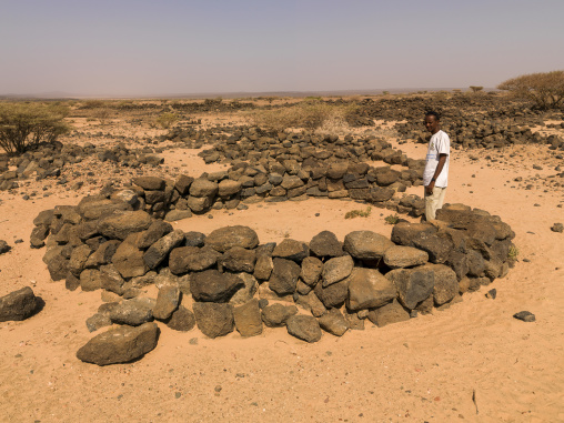 A man stands beside an ancient circular stone grave in the desert landscape, Tadjourah Region, Goubet Al-kharab, Djibouti