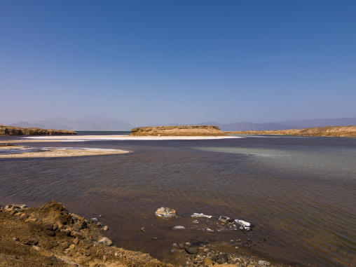 Turquoise water meets white salt flats beneath a distant mountain range, Dikhil Region, Lake Assal, Djibouti