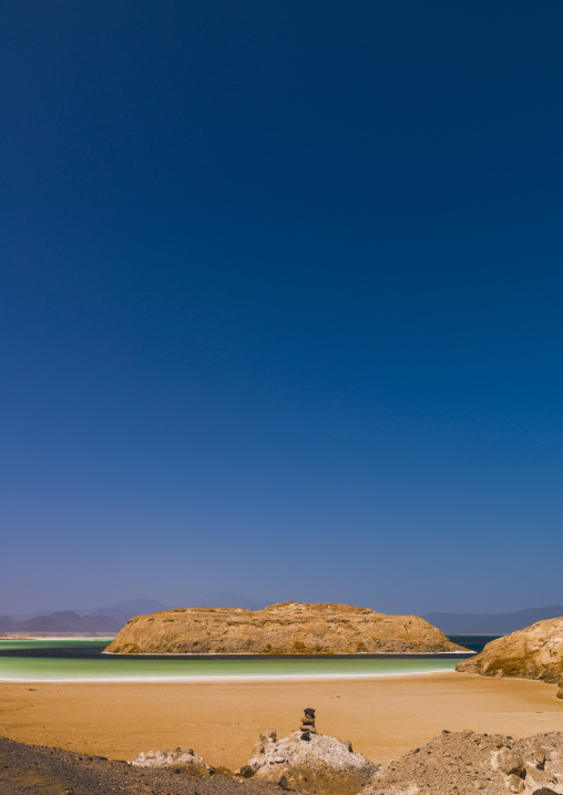 A rocky outcrop rises from turquoise water bordered by white salt deposits, Dikhil Region, Lake Assal, Djibouti