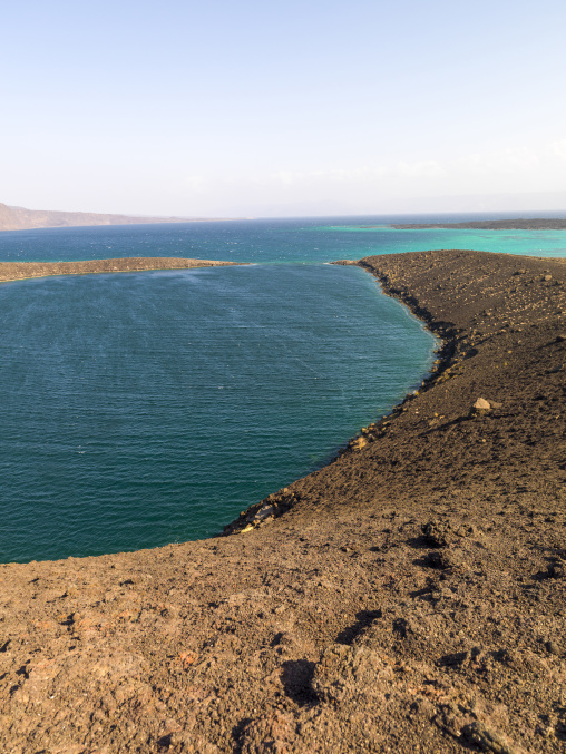 A black volcanic peninsula separates deep blue water from a turquoise lagoon, Tadjourah Region, Goubet Al-kharab, Djibouti