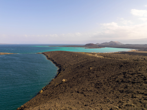 A turquoise lagoon curves along a black volcanic coastline dotted with small huts, Tadjourah Region, Goubet Al-kharab, Djibouti