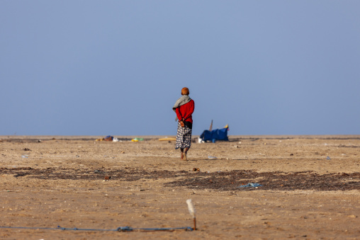 An afar  man in a red shirt walks across a barren coastal plain, Obock Region, Gorodia, Djibouti