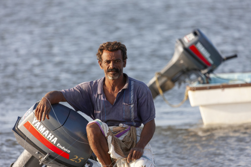 A yemeni fisherman rests beside an outboard motor near the shore, Obock Region, Gorodia, Djibouti