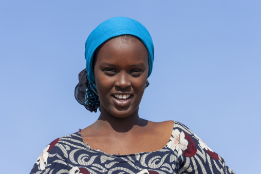 A smiling young afar woman wears a blue headscarf against a clear sky, Obock Region, Khor angar, Djibouti