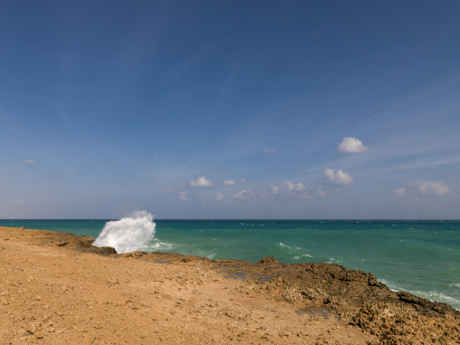 A wave crashes against a rocky shoreline under a clear sky, Obock Region, Khor angar, Djibouti
