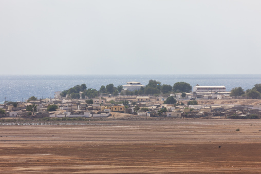 White buildings of a coastal town line the shore beyond a dried mudflat, Obock Region, Obock, Djibouti
