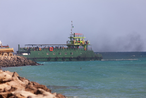 A green passenger ferry arrives near a rocky breakwater in hazy conditions, Obock Region, Obock, Djibouti
