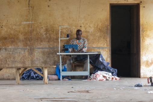 A Senufo tailor sews fabric on a manual sewing machine at his open-air stall, Savanes district, Waraniene, Ivory Coast