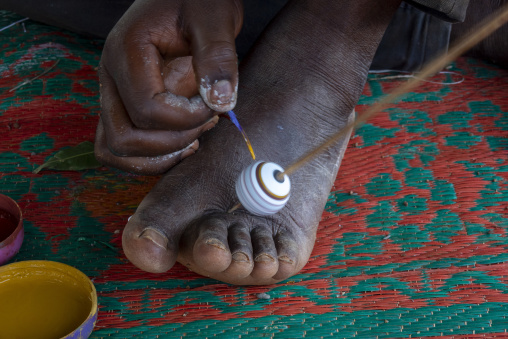 A Senufo craftsman paints colorful stripes onto a clay bead held steady with his foot, Savanes district, Waraniene, Ivory Coast