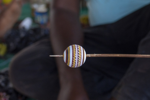 A Senufo craftsman's hand-painted clay bead with striped patterns rests on a wooden stick, Savanes district, Waraniene, Ivory Coast