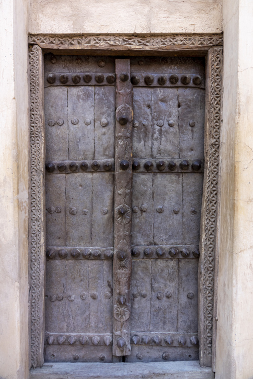 Weathered wooden door with decorative metal studs set in a carved mudbrick doorway, Ad Dakhiliyah Region, Nizwa, Oman