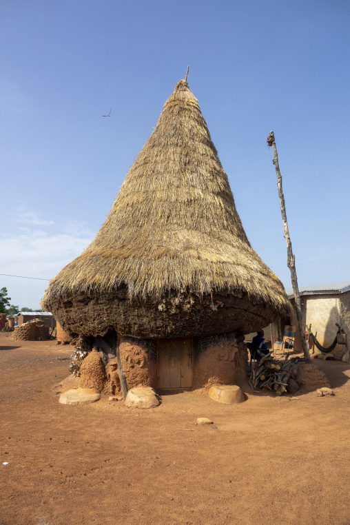 A large conical thatched roof shelters a decorated adobe granary with a carved wooden door in a Senufo village, Savanes district, Niofoin, Ivory Coast