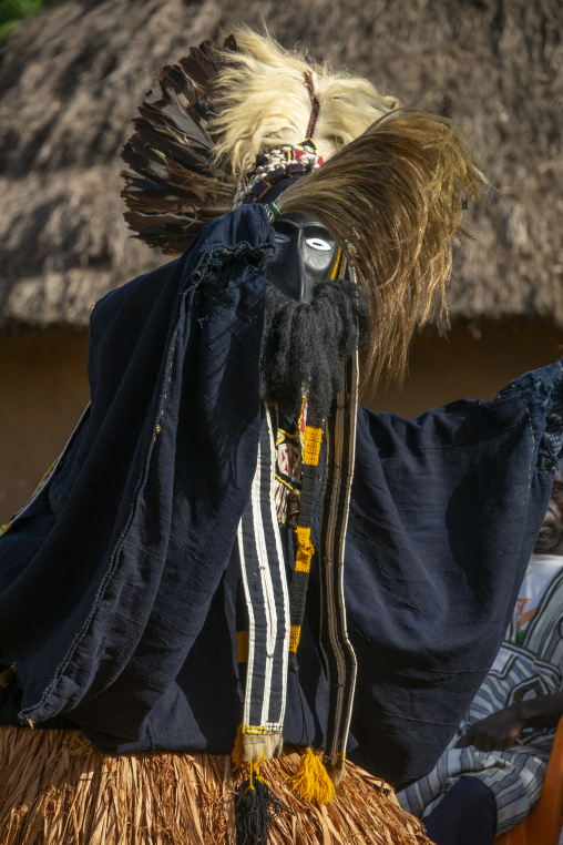 A masked Dan tribe dancer wrapped in a dark robe performs the Kwuya Gblen-Gbe tall mask dance during a ceremony, Bafing, Gboni, Ivory Coast