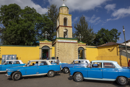 Vintage blue and white Peugeot 404 taxi cars line up in front of a church bell tower, Harari Region, Harar, Ethiopia