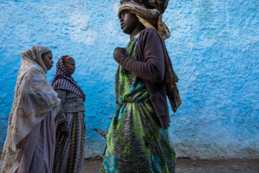 Three women in traditional dress walk past a bright blue wall, Harari Region, Harar, Ethiopia