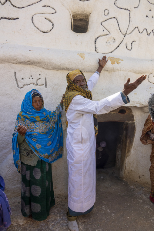 An elderly Sufi pilgrim and a woman touch a sacred wall with their hands raised in prayer, Oromia, Sheik Hussein, Ethiopia