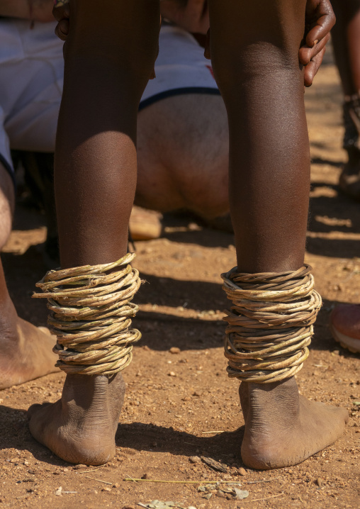 Close-up of two people's legs wrapped in stacked fiber rings above bare feet on red dirt, Cunene Province, Oncocua, Angola