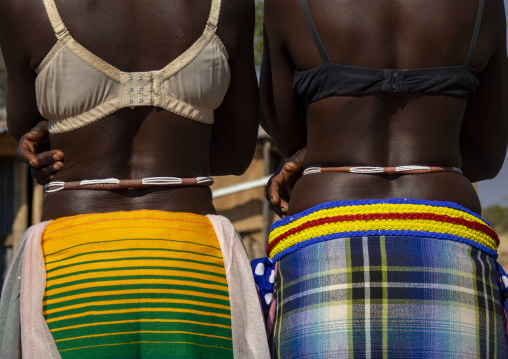 Two women stand side by side from behind wearing lace bras and colorful wrap skirts with beaded belts, Cunene Province, Cahama, Angola