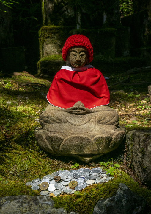 Stone Jizo statue dressed in a red hat and bib surrounded by coi