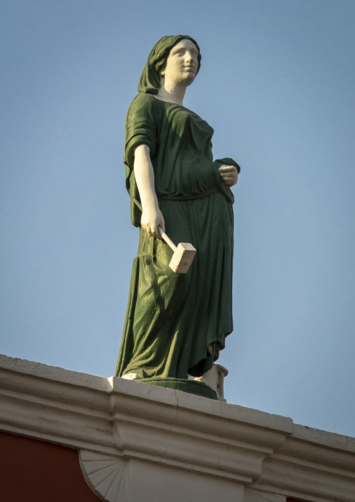Close-up of a painted allegorical statue holding a hammer that symbolizes industry against a clear sky, Luanda Province, Luanda, Angola