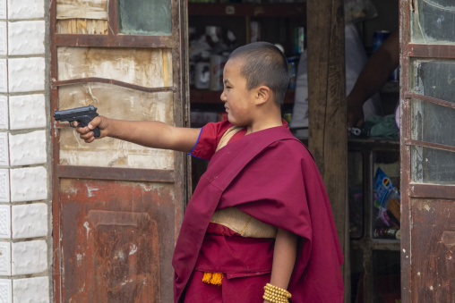 A Tibetan child monk plays with a toy gun at Shachong monastery, Qinghai Province, Wayaotai, China