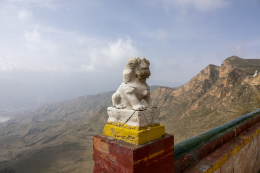 A stone lion statue overlooks the mountains from a wall at Shachong monastery, Qinghai Province, Wayaotai, China