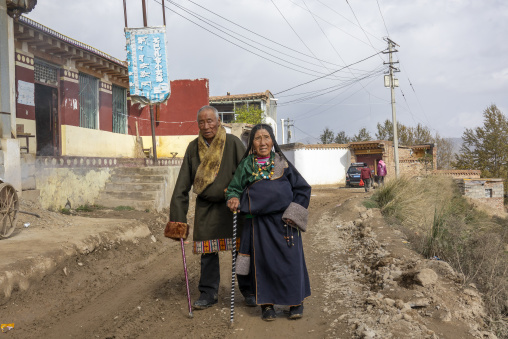 An elderly Tibetan couple walks together on a dirt road near Shachong monastery, Qinghai Province, Wayaotai, China
