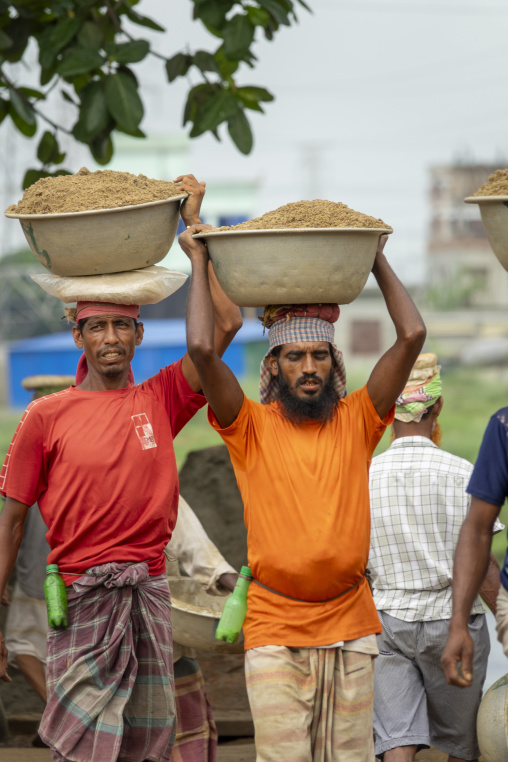 Sand porters carrying heavy metal bowls on their heads at a rive