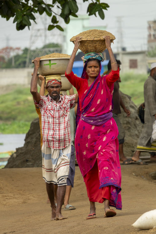 Man and woman carrying baskets of sand on their heads near a hig