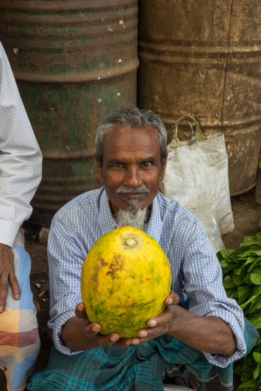 Vendor holding a large yellow pumpkin at a market stall, Dhaka D