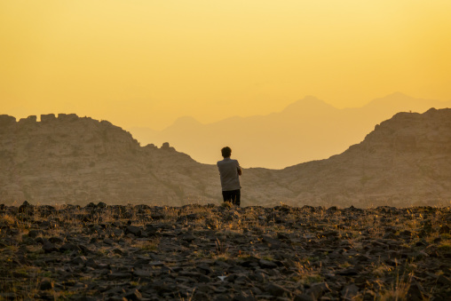 Silhouette of a young man standing on a rocky hilltop at sunset,