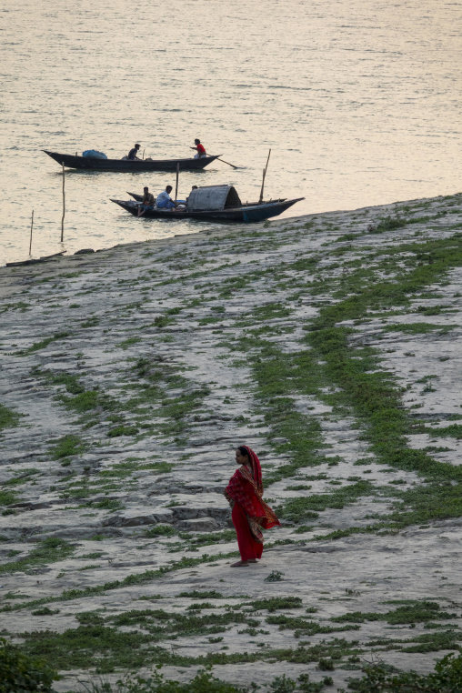 Woman walking along the riverbank with wooden boats on the water
