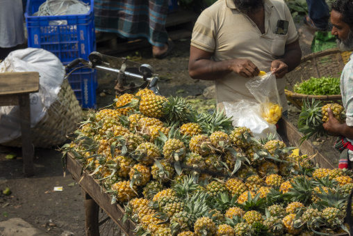 Man bagging fresh pineapple pieces at a market pineapple stall,