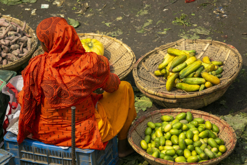 Woman in an orange headscarf sitting beside baskets of cucumbers