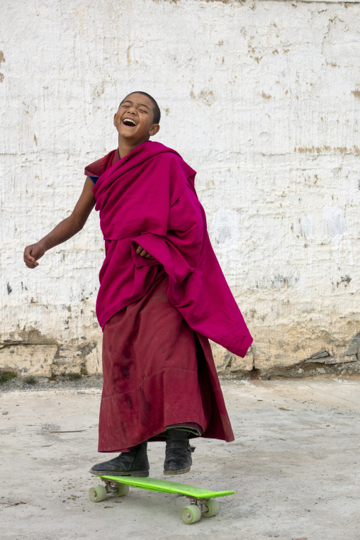 A young Tibetan monk laughs while riding a skateboard at Lhachub monastery, Gansu Province, Lhachub, China