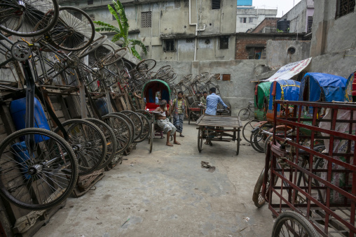 Rows of cycle rickshaw wheels stacked in a repair yard as worker